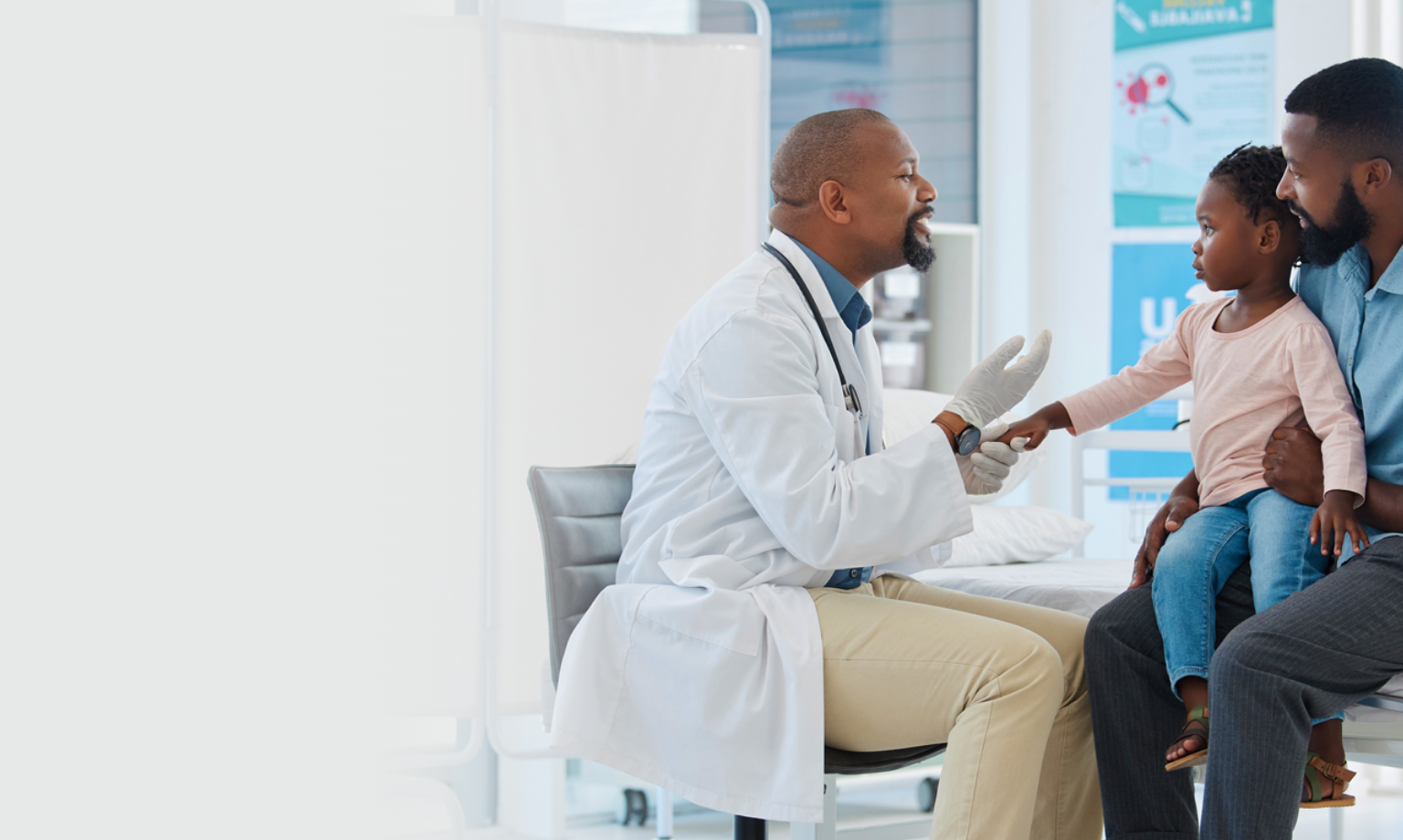 Doctor examines child's hand during check-up while seated on adult's lap in a medical clinic