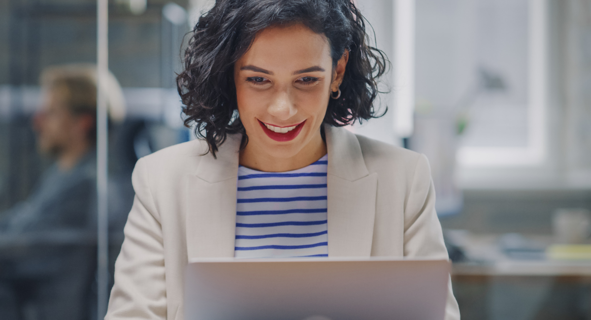 Happy person in blazer and striped shirt working on laptop in office